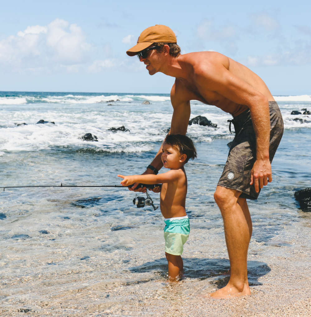 adult male teaching young child to fish at the beach