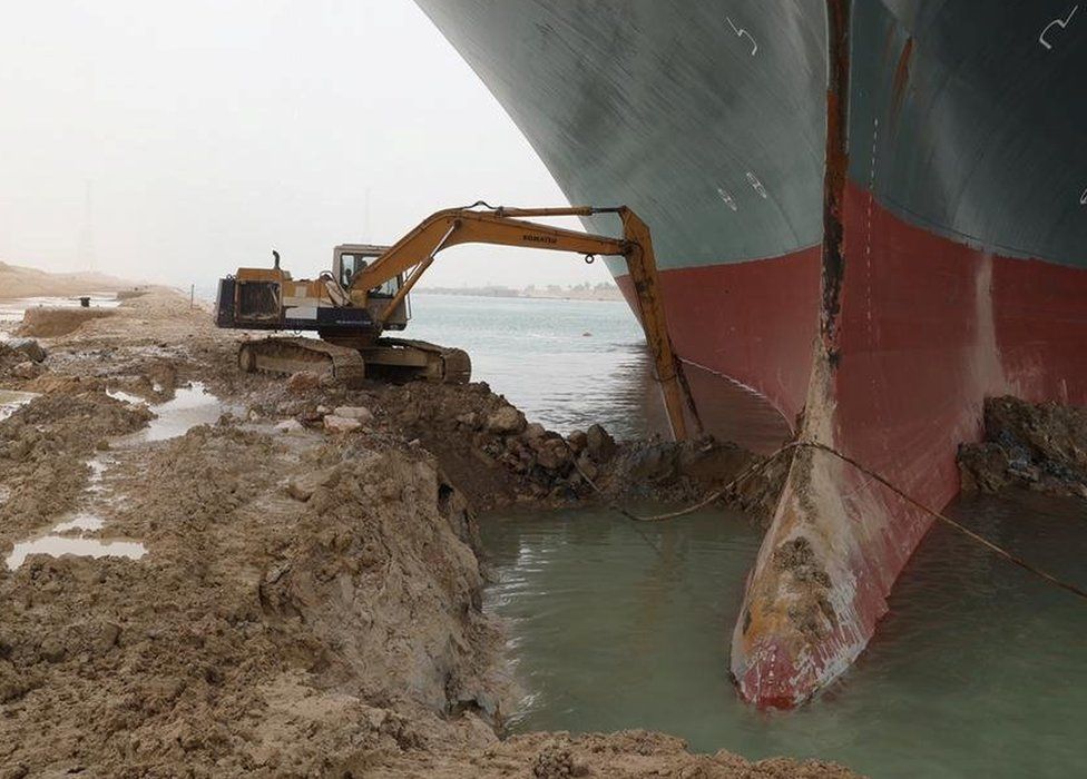Excavator digging out sand around the box of the Ever Given in the Suez Canal, March 2021
