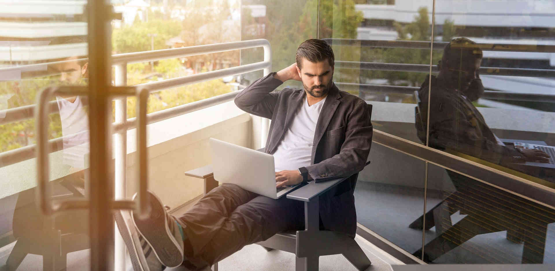 man sitting on gray arm chair using silver laptop computer on building balcony at daytime