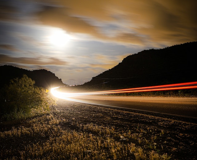 Winding road through desert canyon at sunset, taken at slow shutter speed to create streaks of light from a passing car.