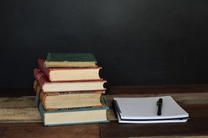 stack of 5 old books next to an open journal with pen