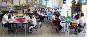 groups of children sitting at tables, coloring, in a classroom setting