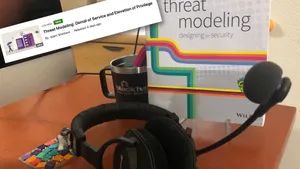 headphones, Threat Modeling book, and mug on a desk with a screen snippet overlay of the Denial of Service and Elevation of Privilege course on LinkedIn