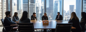 a photograph of hackers at a boardroom table. You can see the concern in their faces. The photo is a corporate publicity shot. The windows overlook a city. There's a package of ‘bomba’ peanut puffs on the table.